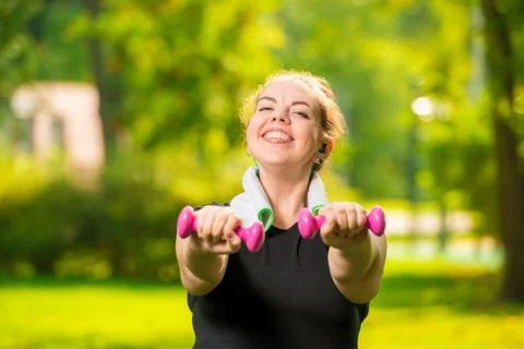Horizontal portrait of a smiling plus size woman with dumbbells in the park d Stock Photos