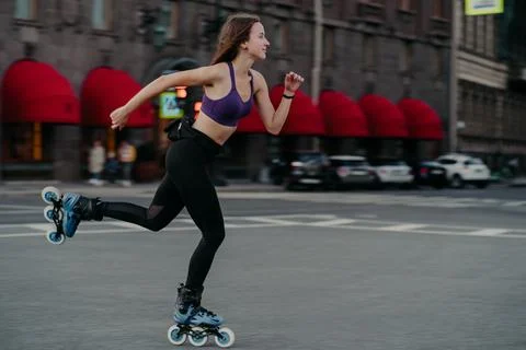Horizontal shot of active slim young woman rides fast on rollerskates improves Stock Photos