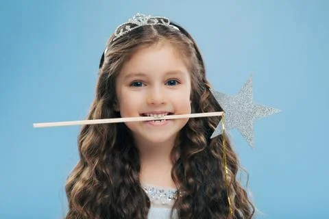 Horizontal shot of attractive smiling small kid holds magic wand in mouth, ha Stock Photos
