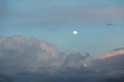 Horizontal shot cumulus clouds float across the evening sky with a full moon on Stock Photos