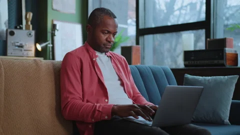 Horizontal shot of focused African American man sitting on sofa and surfing Stock Footage 238748716