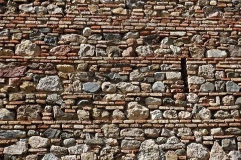 Horizontal stony wall made of thin and thick rows of bricks and stones Stock Photos