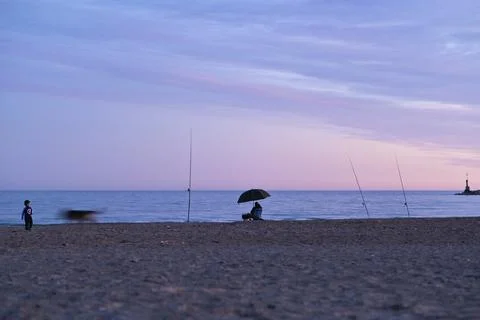 Horizontal tranquil scene at the beach during a blue Fall sunset with fishermen Stock Photos