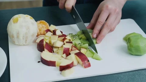 Horizontal video of woman's hands cuts kiwi fruit on a white cutting board for Video stock 136674135