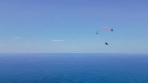 Horizontal wide angle view of a person flying on a paramotor in the blue sk.. Stock Photos