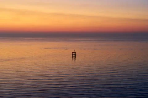 A horizontally oriented view of a wooden structure in a calm sea at sunrise Stock Photos