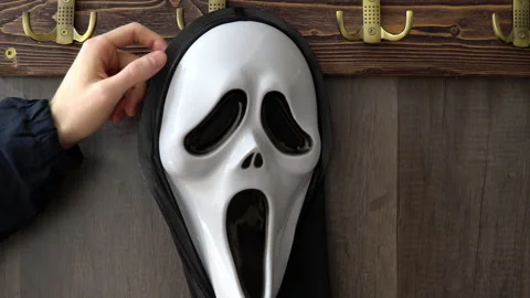 A horrible scream mask hangs on a hook and is taken by a human. A maniac in a Stock Footage 163777557