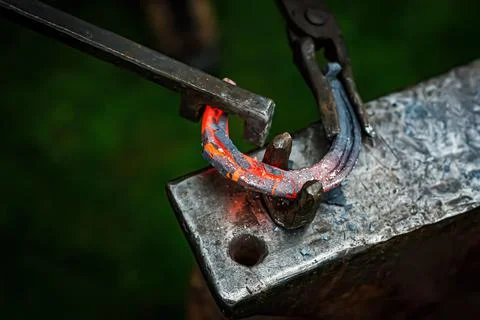 Horseshoe production process. A blacksmith bending hot metal on an anvil. Stock Photos
