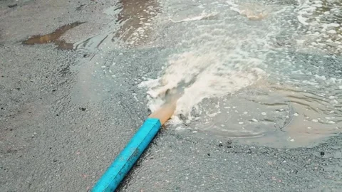 A hose releases water onto a flat surface, causing splashes and forming puddles. Stock Footage 339096035