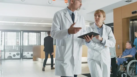 In the Hospital, Busy Doctors Talk, Using Tablet Computer While Walking Through  Stock Footage