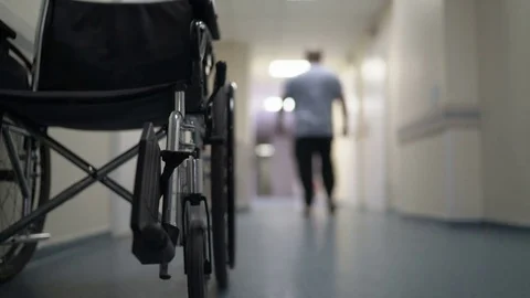 Hospital corridor with empty wheelchair and man walking away Stock Footage