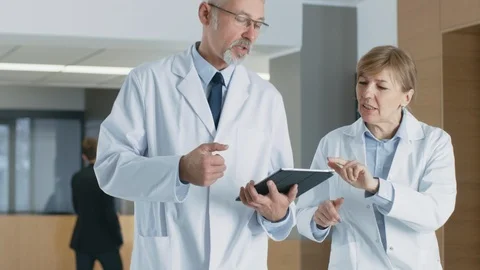 In the Hospital Doctors Walking through Lobby have Discussion while Using Tablet Stock Footage 90171925
