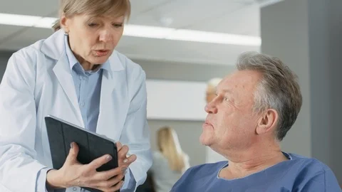 In the Hospital Female Doctor Shows Tablet Computer to Elderly Patient Stock Footage
