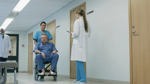  Hospital Hallway Nurse Pushes Wheelchair with Old Man Doctor Asks Qu Stock Footage