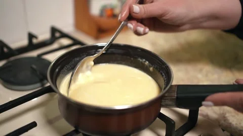 The hostess is preparing dough in the kitchen. He heats the liquid on gas in a Stock Footage 253486661