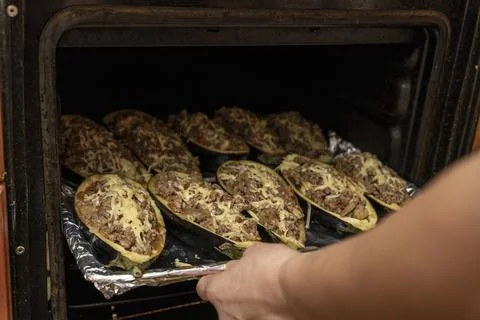 Hostess puts a baking tray with eggplant stuffed with meat in the oven Foto stock