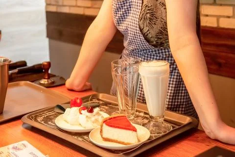 The hostess of a small cafe prepares an order of cheesecake dessert and milks Stock Photos