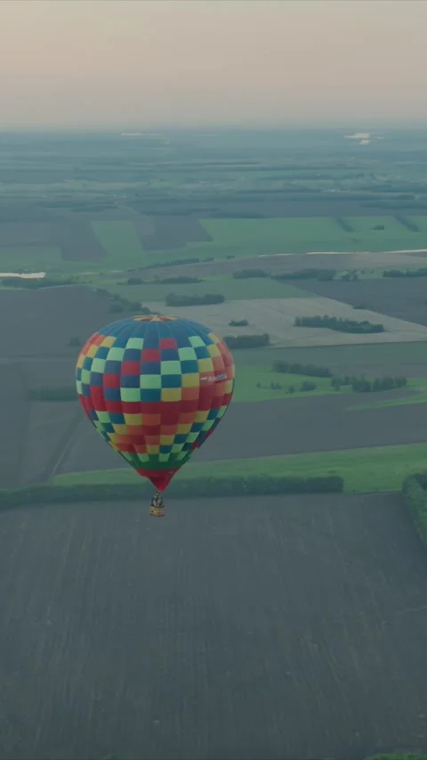 Hot air balloon with checkered pattern floats over patchwork fields and greenery Stock Footage 348250592
