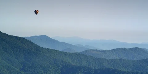 Hot air balloon floating over the mountains covered with green forest Stock Footage 103750682