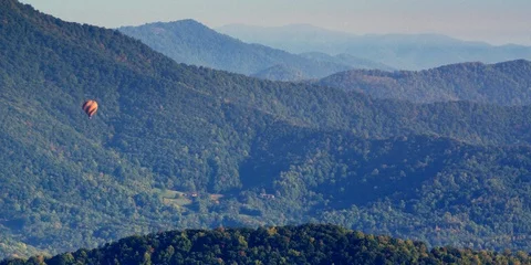 Hot air balloon floating over the mountains covered with green forest Stock Footage 103751555