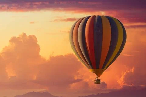 A hot air balloon rising under partly cloudy skies during a brillant sunset Stock Photos