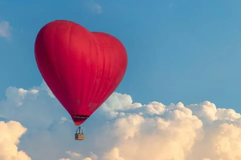 A hot air balloon in the shape of a red heart flies above the clouds. Unusual Stock Photos