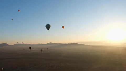 Hot air balloons float over a vast desert landscape at sunrise Stock Footage 297987915