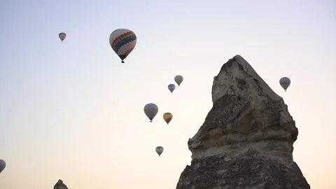 Hot air balloons float in sky while birds fly over rock Stock Footage 146576014