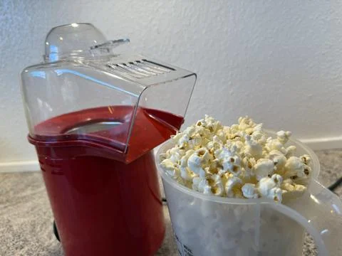 Hot air popcorn maker next to a full measuring cup of fresh popcorn on a ki.. Stock Photos