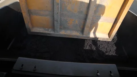 Hot asphalt concrete falling from dump truck into hopper of paver Stock Footage 158040835