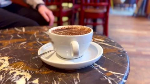 Hot beverage coffee in white cup with saucer and teaspoon on coffee shop table Stock Footage 336469685