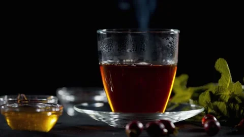 Hot black tea in the cup on the table with honey, rosehip and mint leaves, 4k Stock Footage 141570468