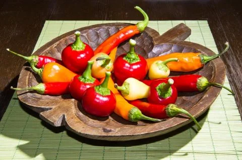 Hot chilli pepers of different colors and flavours on a wooden plate Stock Photos