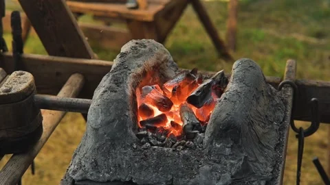 Hot coal glows brightly in a forge as a blacksmith works with metal tools. The Stock Footage 345036884