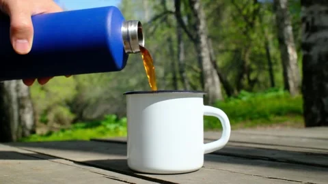 Hot coffee being poured from blue thermos flask into white enamel mug 库存影片 333586053