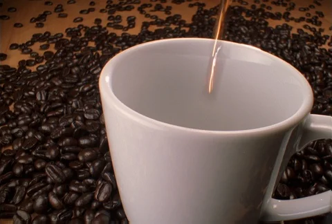 Hot coffee being poured into a cup resting on coffee beans Video stock 86883729