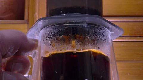 Hot coffee being pushed down a cylindrical chamber to drip into a glass cup. Stock Footage 300682667