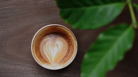 Hot coffee cup with heart shape latte art and green coffee leaves Stock-Footage 120548567