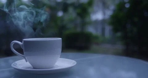 Hot Coffee or Tea Cup with Vapour steam coming out. Green plants in background Stock Footage 172107789
