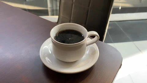 Hot coffee in a white cup placed on the corner of a wooden table Vidéo 346838432