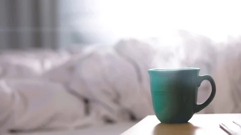 Hot cup of coffee on night table and messy bed 4K Stock Footage 99432725