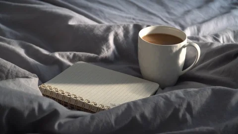 Hot cup of coffee with notebook and pencil on a bed. 库存影片 112509192