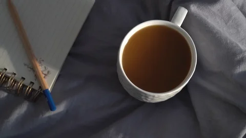Hot cup of coffee with notebook and pencil on a bed. Cozy hygge, lagom scene. 库存影片 112509415