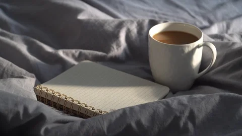 Hot cup of coffee with notebook and pencil on a bed. Cozy hygge, lagom scene. 動画素材 112509558