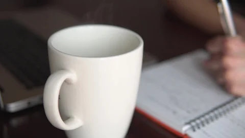 Hot cup with computer and a man writing with pen Stock Footage 129440018