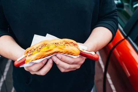 Hot dog in the hands of a guy standing by the car Stock Photos
