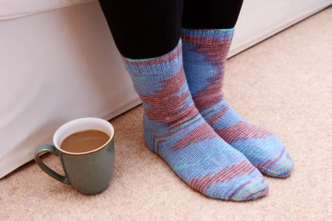 Hot drink on the floor by feet in socks Stock Photos