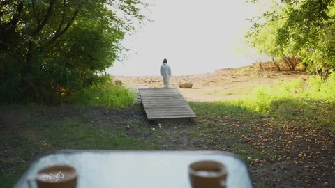 A hot drink in two cups on a table in a garden landscape. Girl in the background Stock Footage 255459439