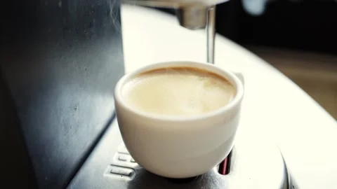 Hot espresso brewing in a white cup from a coffee machine with steam rising Stock Footage 339000601