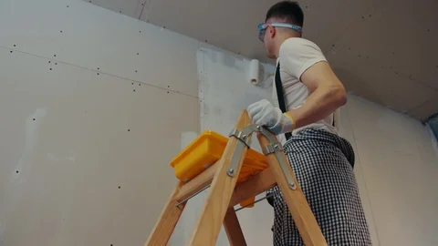 Hot house painter stands on the ladder, actively paints the wall. Sexy builders Stock Footage 87387635